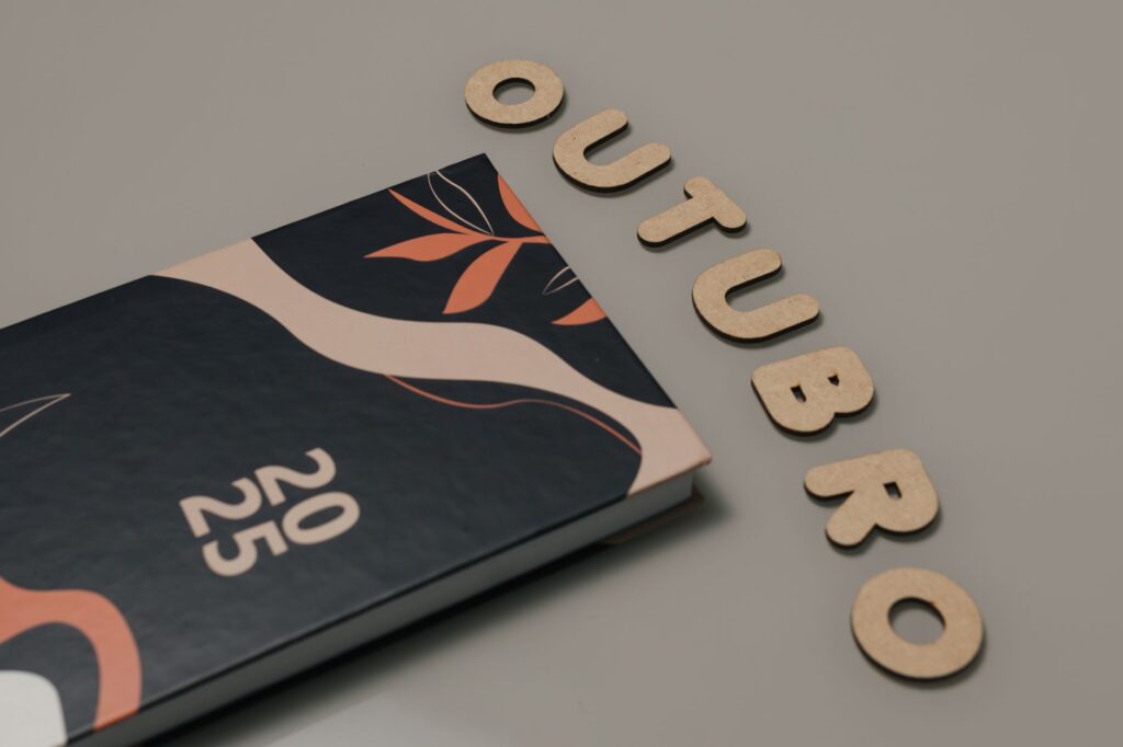 Minimalist flat lay featuring a 2025 planner and cut-out letters spelling 'OUTUBRO'.