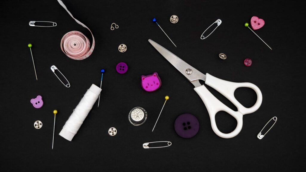 Flat lay of various sewing tools including scissors, pins, and buttons on a black background.