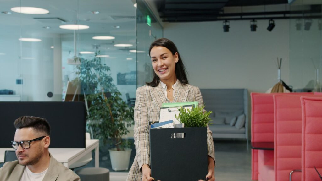 Happy businesswoman carrying belongings and plant into a modern office.