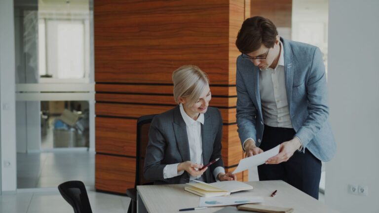 Two professionals discussing documents in a modern office setting.