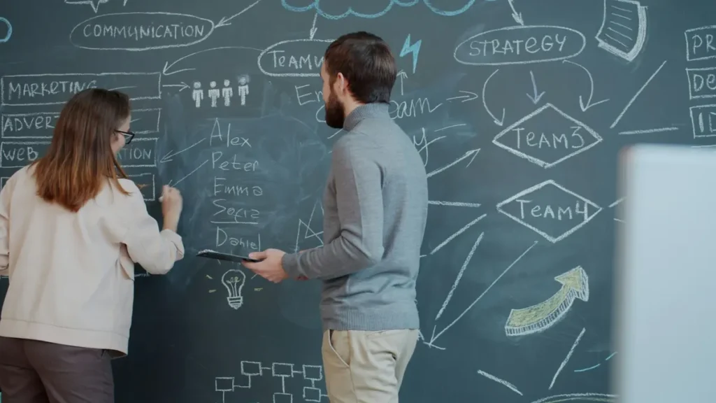 Two people planning on a chalkboard with diagrams.