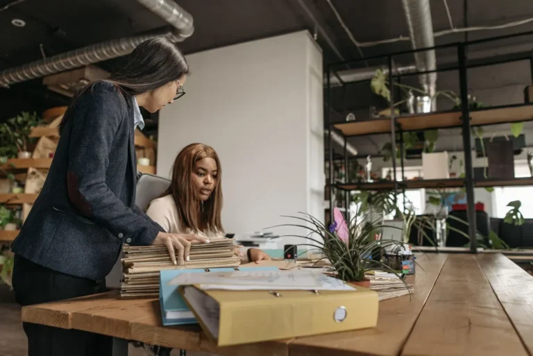 Two diverse businesswomen collaborating over documents in a modern office setting.