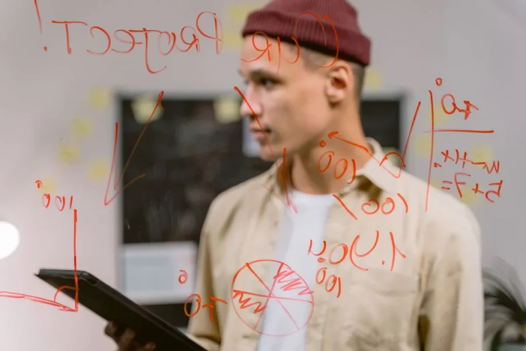 Man strategizing ideas on a glass panel with red marker writings, creating an innovative brainstorming session.