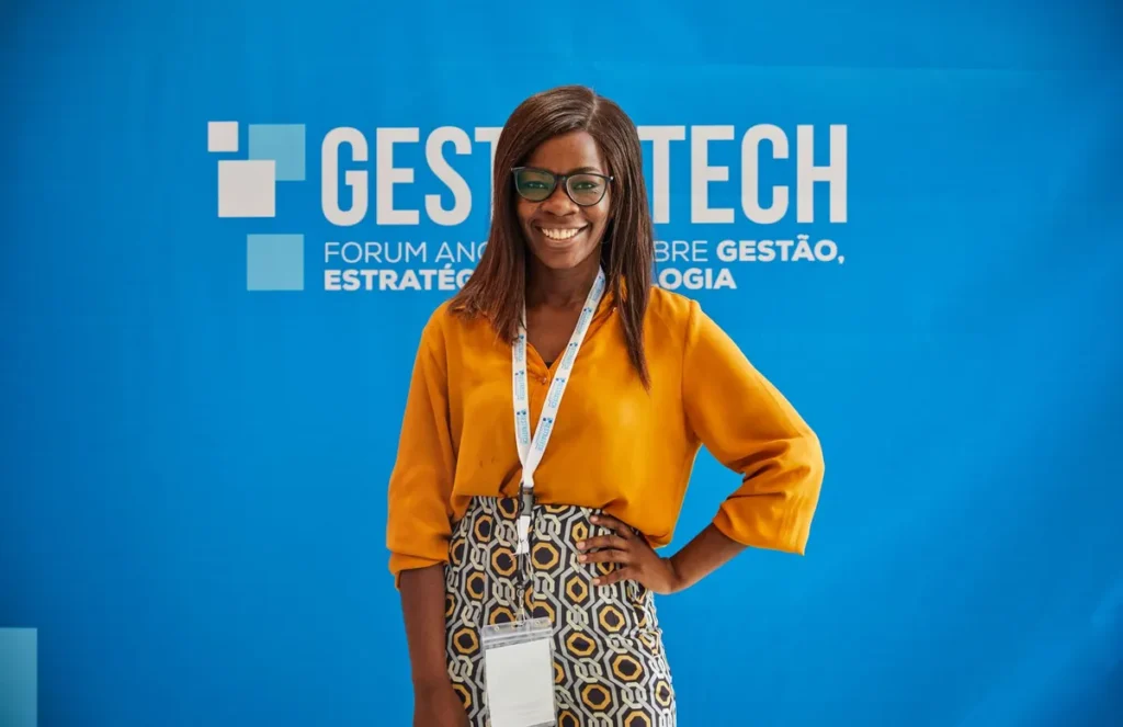 Smiling woman in orange blouse poses confidently at Gest Tech event backdrop.