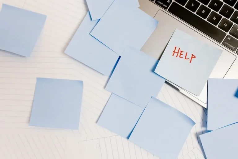 A cluttered workspace with sticky notes on a laptop, symbolizing overwhelm and need for help.