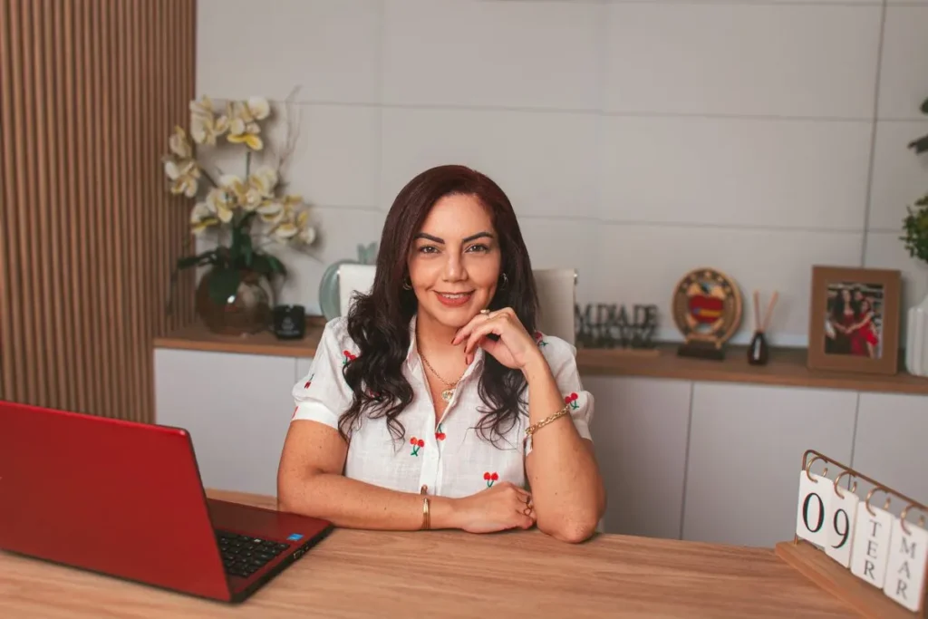 Professional woman smiling at desk with red laptop in a stylish workspace.