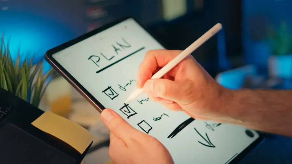 Person using a digital tablet and stylus to plan and organize tasks in an office setting.